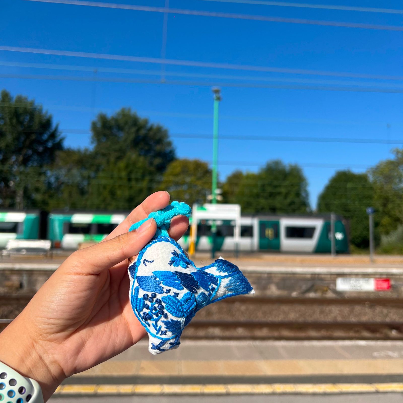 Small blue batik pouch held up in front of a tram