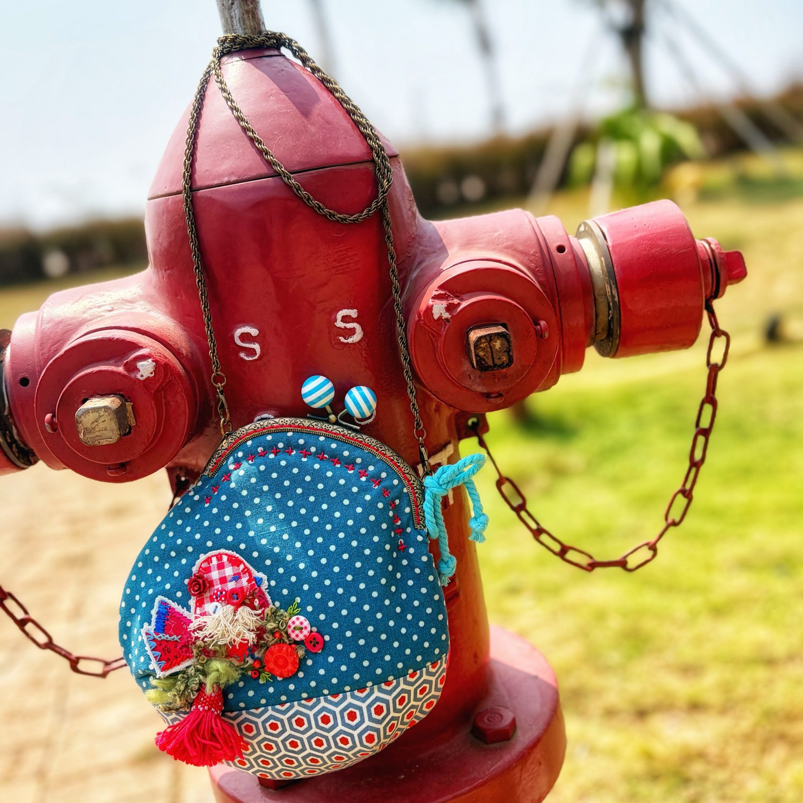 Blue patchwork kiss-lock pouch with a chain, hanging off a red fire hydrant